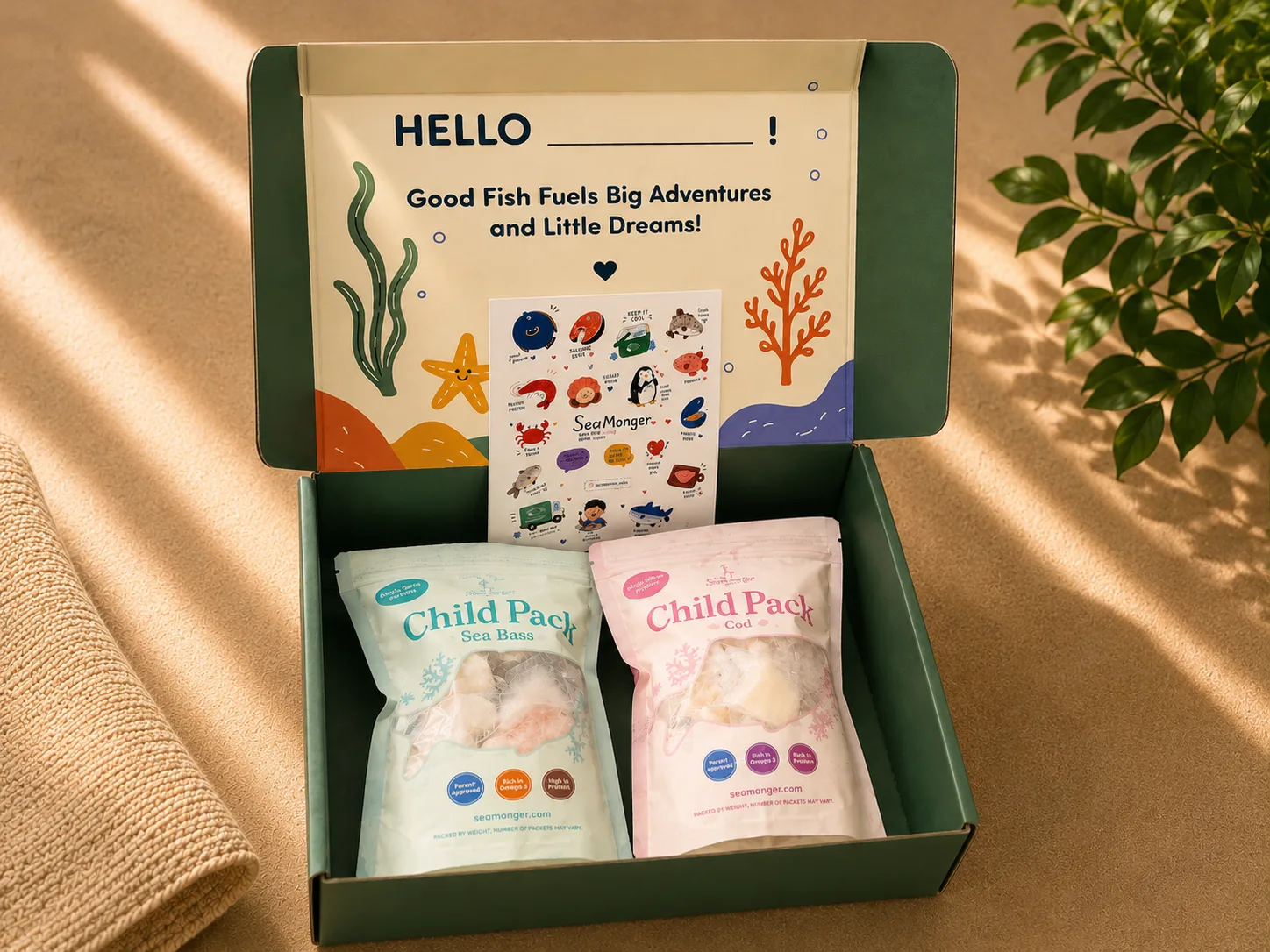 An opened Little SeaMonger Collection box: a printed card reading “Good Fish Fuels Big Adventures and Little Dreams”, a sticker sheet, and two Child Pack pouches — sea bass and cod.